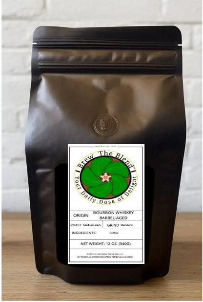 A matte black resealable coffee bag with a white label reading 'The Blend' and 'Bourbon Whiskey Barrel-Aged,' standing on a wooden surface against a white brick wall.